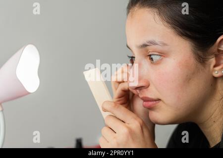 jeune latina femme se concentrant se regardant dans le miroir tout en mettant sur les faux cils Banque D'Images