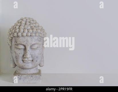 Gros plan de la statuette en céramique d'une tête de Bouddha sur fond gris avec espace de copie. Banque D'Images