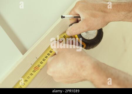 Gros plan sur la mesure de ruban d'un menuisier lorsqu'il mesure un morceau de bois qu'il utilisera plus tard dans son atelier de travail du bois Banque D'Images