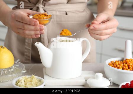 Femme qui fait une boisson stimulant l'immunité avec de la poudre curcuma à table en marbre, gros plan Banque D'Images