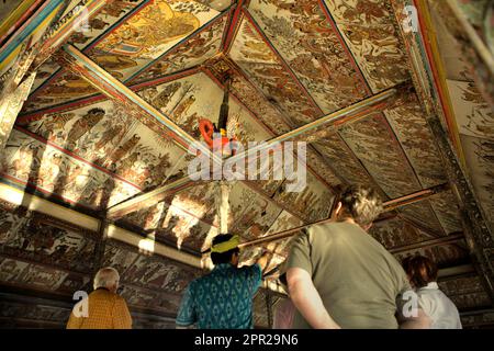 Un guide explique à un groupe de touristes sur l'ancienne peinture de style kamasan sur les plafonds du pavillon Kertha Gosa, une ancienne salle de réunion où les dirigeants traditionnels ont discuté des questions de justice, situé dans la zone du complexe du palais de Klungkung aboli à Semarapura, Klungkung, Bali, Indonésie. Banque D'Images