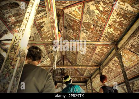 Un guide explique à un groupe de touristes sur l'ancienne peinture de style kamasan sur les plafonds du pavillon Kertha Gosa, une ancienne salle de réunion où les dirigeants traditionnels ont discuté des questions de justice, situé dans la zone du complexe du palais de Klungkung aboli à Semarapura, Klungkung, Bali, Indonésie. Banque D'Images