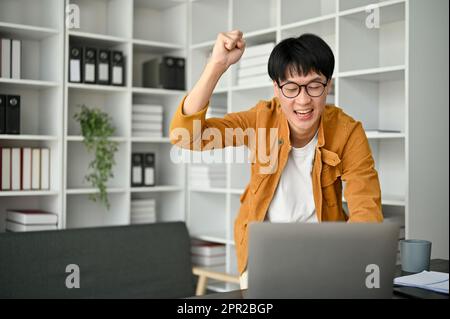 Image d'un jeune homme qui célèbre tout en regardant l'écran d'ordinateur portable après avoir entendu une bonne nouvelle. Banque D'Images