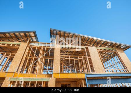 Vue en angle bas de la charpente en bois d'une maison à plusieurs étages en construction, avec ses toits inclinés et un ciel sans nuages au-dessus Banque D'Images