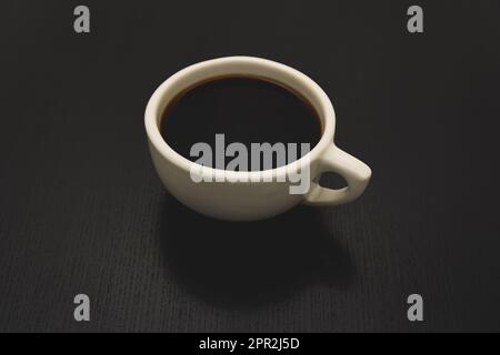 Un café noir dans une tasse blanche classique de style américain est posé sur une table noire. Banque D'Images