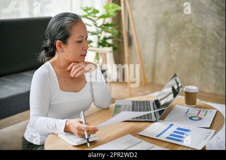 Femme d'affaires sénior travaillant à domicile, travaillant sur ses rapports financiers dans son salon. Banque D'Images