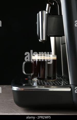 Machine à espresso moderne avec une tasse de café en verre sur une table grise sur fond noir Banque D'Images