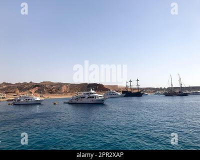 Une variété de bateaux à moteur et à voile, de bateaux, de paquebots de croisière se trouvent sur un quai dans le port sur le fond de la mer bleue et de la montagne de pierre brune Banque D'Images