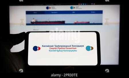 Personne tenant un téléphone mobile avec le logo du Consortium de pipeline Caspian (CPC) à l'écran en face de la page Web. Mise au point sur l'affichage du téléphone. Banque D'Images