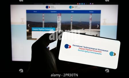 Personne tenant un téléphone portable avec le logo de Caspian Pipeline Consortium (CPC) à l'écran en face de la page Web des affaires. Mise au point sur l'affichage du téléphone. Banque D'Images