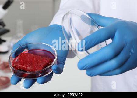 Scientifique tenant en laboratoire une boîte de Pétri contenant de la viande de culture crue, en gros plan Banque D'Images