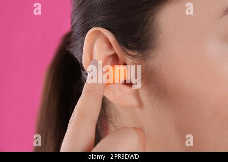 Jeune femme insérant un bouchon d'oreille en mousse sur fond rose, gros plan Banque D'Images