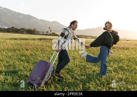 Un jeune couple épris inspiré regarde le plan de vie à l'avenir. Ils sont debout avec une valise et ukulele, tenant les mains. Recherche d'une nouvelle homela Banque D'Images