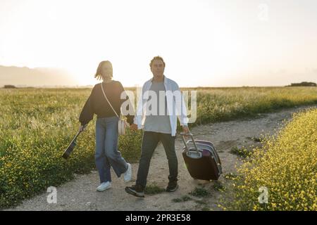 Un jeune couple épris inspiré regarde le plan de vie à l'avenir. Ils sont debout avec une valise et ukulele, tenant les mains. Recherche d'une nouvelle homela Banque D'Images