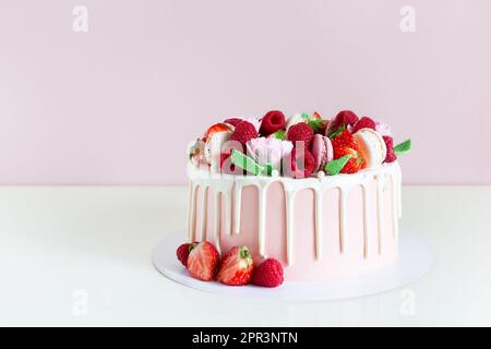 Gâteau d'anniversaire sucré avec baies, macaron et décoration florale sur la table. Magnifique gâteau rose décoré de macarons, framboises, fraises et sucre Banque D'Images