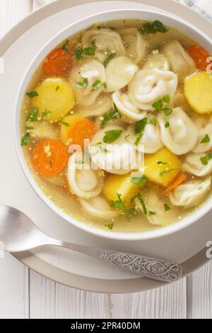 Soupe aux boulettes de viande russe pelmeni, pommes de terre et autres légumes sur le bol de la table en bois. Vue verticale du dessus Banque D'Images
