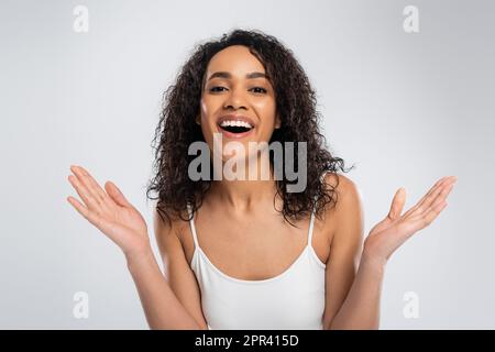 impressionnée afro-américaine femme avec des cheveux de brunette ondulés montrant le geste de wow et regardant la caméra isolée sur gris, image de stock Banque D'Images