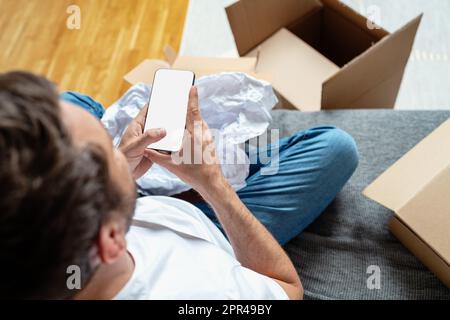 Téléphone mobile avec écran vierge dans les mains des hommes, cartons sur l'arrière-plan. Banque D'Images