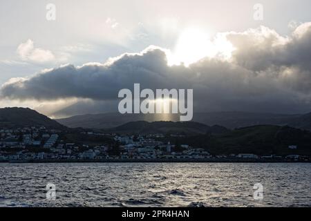 Le soleil se couche derrière les nuages au-dessus de la ville de Madalena, île de Pico, Açores, Portugal Banque D'Images