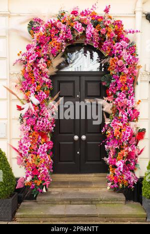 Fausses fleurs en plastique imitation, guirlande de fleurs, encadrement de porte avant noir ou gris foncé, avec des meubles de porte en laiton et une marche en pierre. Cheltenham, Angleterre. ROYAUME-UNI. (134) Banque D'Images