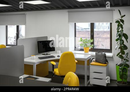 Bureau informatique avec espaces de travail pour les employés développeurs avec chaises jaunes et ordinateur. Banque D'Images