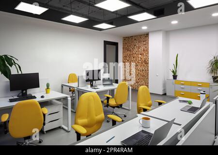 Bureau informatique avec espaces de travail pour les employés développeurs avec chaises jaunes et ordinateurs. Banque D'Images