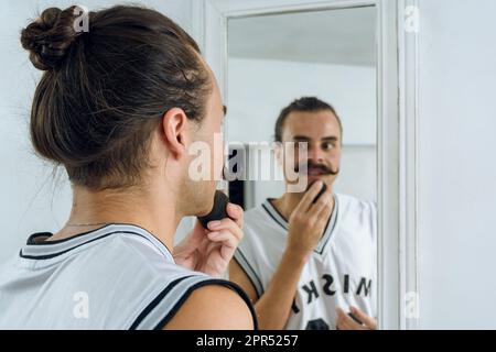 jeune hispanique latina sexe non binaire personne debout devant un miroir appliquant le maquillage appliquer la fondation avec une éponge., se concentrer sur le premier plan Banque D'Images