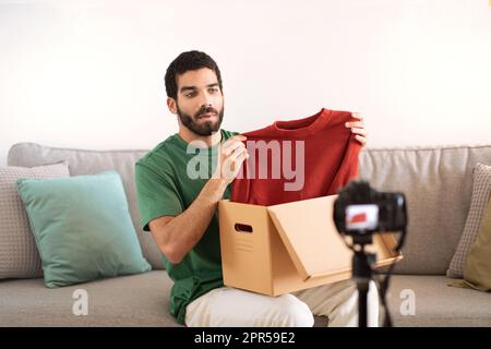 Un blogueur sérieux jeune moyen-oriental avec boîte en carton montre des vêtements, tournage vidéo Banque D'Images