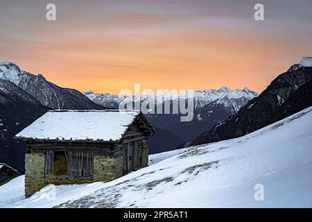 Refuge de montagne isolé dans une neige profonde avec des sommets enneigés à l'aube, Tombal, Val Bregaglia, Graubunden, Suisse Banque D'Images