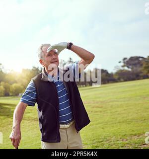 J'ai eu une certaine distance sur ce dernier. un homme âgé qui protège ses yeux du soleil tout en jouant au golf. Banque D'Images