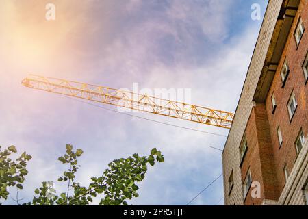 La façade d'une maison résidentielle moderne en brique et la flèche d'une grue de construction - le concept de construction de logements et d'investissement immobilier Banque D'Images