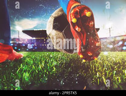 Scène de nuit football match avec gros plan d'une chaussure de soccer frapper la balle avec puissance Banque D'Images