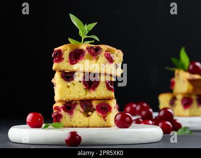 Morceaux de gâteau de Savoie cuits avec des cerises mûres rouges sur un panneau de bois blanc Banque D'Images