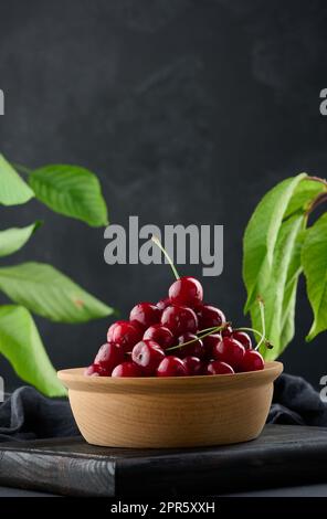 Cerises rouges mûres dans une assiette en bois sur une table noire Banque D'Images