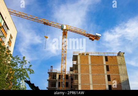 Construction tour grue sur le site de construction d'un immeuble résidentiel moderne en briques, sur fond de lumière du soleil, lever du soleil, été Banque D'Images