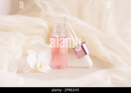 Bouteille de Dropper rose près de la fleur d'orchidée blanche sur fond jaune clair. Produit de beauté pour les soins de la peau Banque D'Images