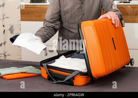 Un homme plie les objets dans une valise de voyage de couleur orange sur roues. Préparation du voyage. Banque D'Images