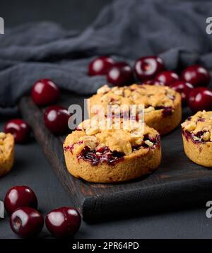 Portion de tarte crumble avec cerises sur un panneau de bois décoré de feuilles de menthe verte, fond noir Banque D'Images