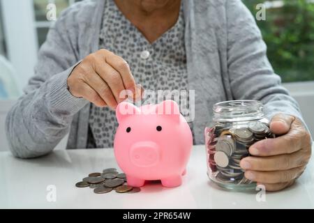 Femme asiatique âgée ou âgée tenant compte de l'argent de pièce dans la banque de piggy. Pauvreté, problème d'épargne à la retraite. Pauvreté, problème d'épargne à la retraite. Banque D'Images