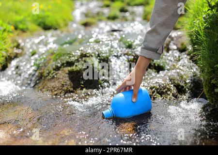 Randonneur à la main remplissant la cantine avec de l'eau de rivière Banque D'Images