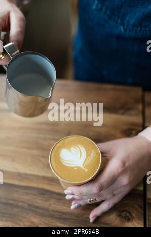 Le processus de fabrication d'un cappuccino Barista avec un beau motif sous la forme d'un coeur sur la mousse dans un verre éco-artisanal. Concept café à emporter. Banque D'Images