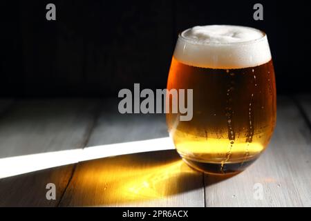 Une bière mousseuse versée dans un verre court et arrondi illuminé par la forte lumière de l'après-midi Banque D'Images