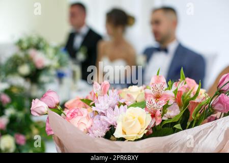 Bouquet de fleurs roses sur le fond de la mariée et du marié flou et de leurs invités. Banque D'Images