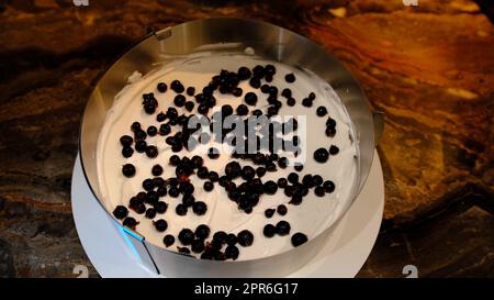 un chef pâtissier met un gâteau sur une crème aux myrtilles et le presse. Aplatit et aplatit le gâteau en gros plan Banque D'Images