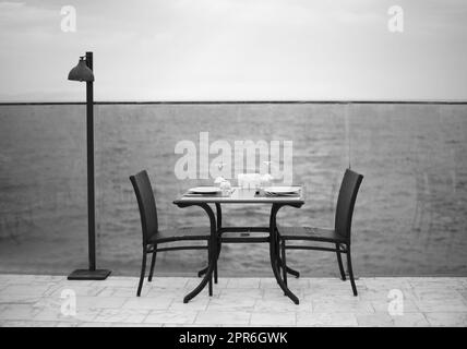 Dîner romantique incroyable sur la plage. Romance et amour, table à manger avec vue sur la mer par temps nuageux. Photo noir et blanc Banque D'Images