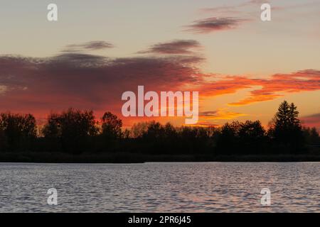 Nuages rouges orangés après le coucher du soleil sur les arbres et le lac Banque D'Images