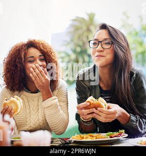 Partager de la bonne nourriture et de bonnes blagues. Photo de deux petites amies mangeant des hamburgers à l'extérieur. Banque D'Images