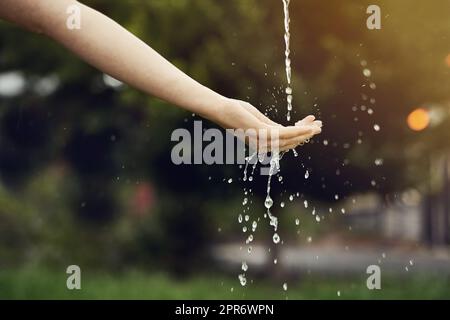 Chaque goutte compte. Coupe courte d'eau sur une main de femme à l'extérieur. Banque D'Images