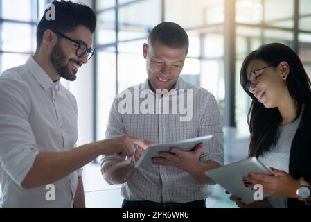 Synchronisation de leurs appareils. Prise de vue de trois collègues utilisant des tablettes numériques dans un bureau. Banque D'Images