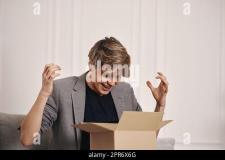 homme assis sur le canapé et déballant la boîte en carton. Banque D'Images